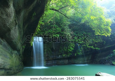 A cool refreshing waterfall tumbling down the cliff into an emerald pond hidden in a mysterious forest of lush greenery. Beautiful river scenery of Taiwan in springtime.