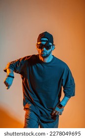 Cool serious dancer man with sunglasses and a cap in a trendy t-shirt is dancing in a creative color studio with orange and neon lights - Shutterstock ID 2278049695