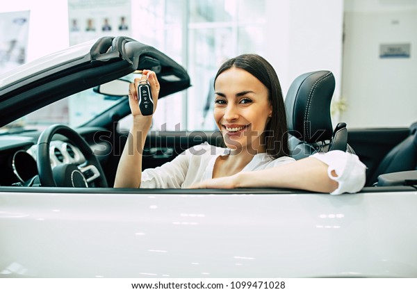 Cool sport woman car. Smiling gorgeous\
woman shows car key on camera at the\
dealership