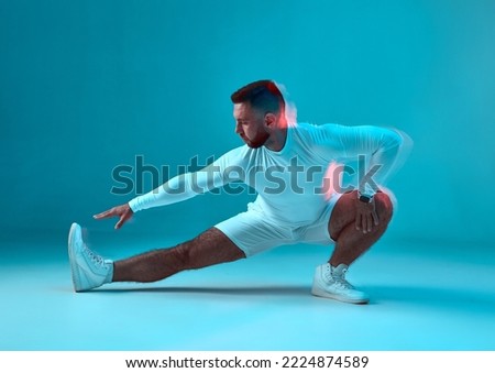 Cool sportive guy stretching leg on floor on blue studio background. Sport club advertisement. Gym, athletic training