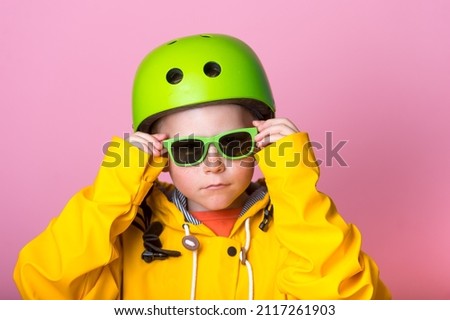 Cool stylish kid boy in sunglasses and helmet look in camera isolated on pink. Funny child boy in yellow bright clothes ready to do sport