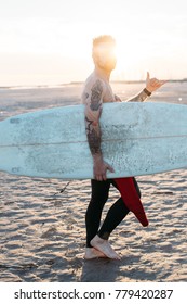 Cool And Stylish, Trendy Surfer Walks On Beach At Sunset Or Sunrise Before Catching Wave, Hangs Ten Or Shows Sign With Hand Of Hang Ten, Millennial Or Hipster Startup Relaxed Chill Lifestyle In Goa