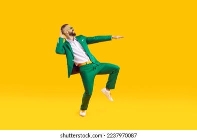 Cool and stylish young man is having fun dancing celebrating Saint Patricks Day. Caucasian man in stylish green suit, white shirt and sunglasses smiling while dancing on orange background. Web banner - Powered by Shutterstock