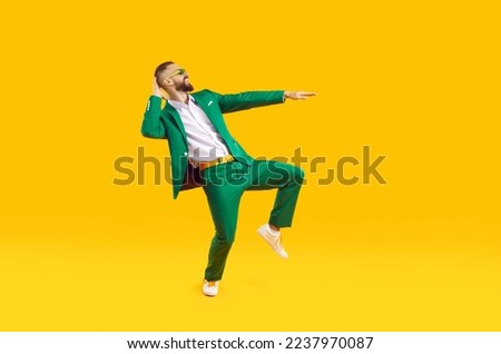 Cool and stylish young man is having fun dancing celebrating Saint Patricks Day. Caucasian man in stylish green suit, white shirt and sunglasses smiling while dancing on orange background. Web banner