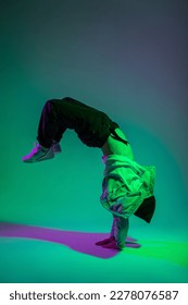 Cool stylish young professional dancer man b-boy in trendy fashion denim clothes with sneakers is dancing and freeze on hands in a creative color studio with pink and green light. Dance in motion - Shutterstock ID 2278076587