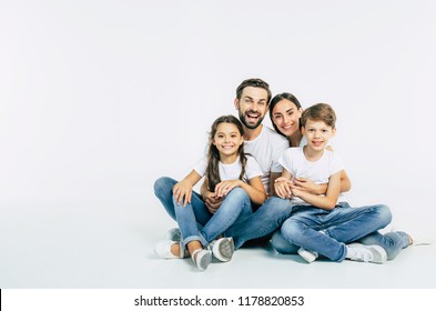 Cool team. Beautiful and happy smiling young family in white T-shirts are hugging and have a fun time together while sitting on the floor and looking on camera. - Shutterstock ID 1178820853