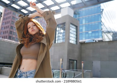 Cool teen stylish redhead fashion hipster girl model posing in big city urban location. Beautiful teenage generation z girl with red hair wearing trench coat looking at camera. Portrait - Shutterstock ID 2189880561