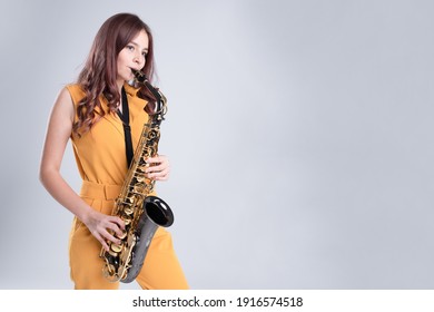 Cool teenage girl playing saxophone. Young woman musician in yellow clothes with gold sax on gray studio background. Concept of hobbies, inner world, development of talents, music school. Copy space.