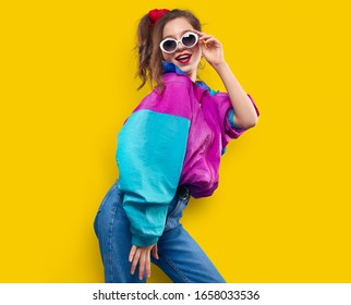 Cool teenager. Fashionable DJ girl in colorful trendy jacket and vintage retro sunglasses enjoys style of 80s - 90s vibes. Teenager Girl at disco party. Young fashion model on yellow color background.