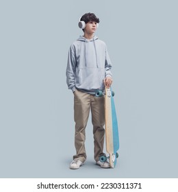 Cool teenager posing with a skateboard, isolated on gray background