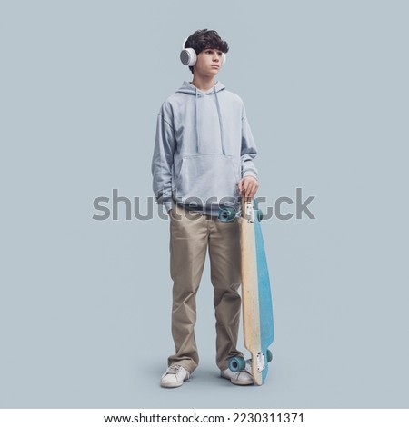 Cool teenager posing with a skateboard, isolated on gray background