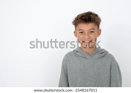 cool young 12 year old boy with grey hoody sweater posing in front of white background, having fun