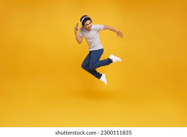 Cool young asian man jumping isolated on yellow background studio portrait. Listening music with headphones, dancing. People lifestyle concept.