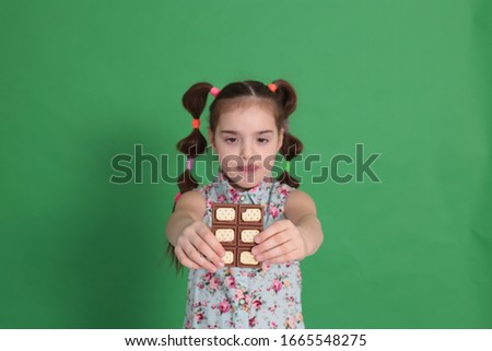 Cool young beautiful girl of eight years old with a funny hairstyle, in a wonderful mood, eats chocolate with cookies on a bright green background