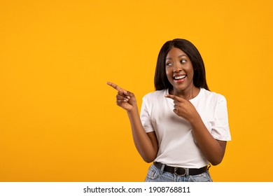 Cool Young Black Woman Pointing And Looking At Copy Space Over Yellow Studio Background, Positive African American Lady Showing Exciting Text Or Advertisement, Recommending Some Product