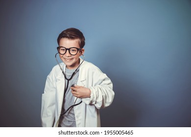 Cool Young Boy Is Disguised As A Doctor With A White Doctor Smock And Plays With Syringe And Stethoscope In Front Of Blue Background