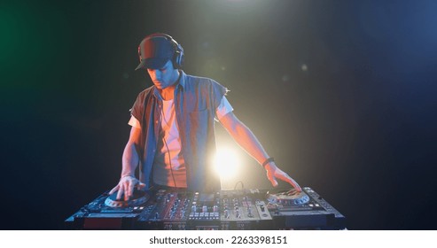 A cool young dj approaches the mixer controller and puts headphones on, ready to perform in a nightclub - nightlife concept  - Shutterstock ID 2263398151