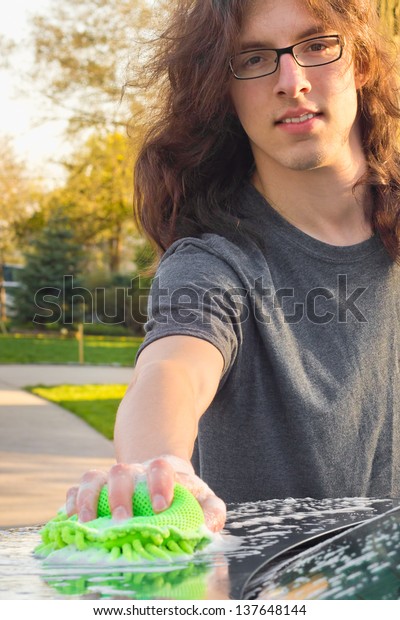Cool\
young guy with long hair washing car on a spring\
day