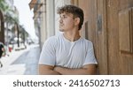 Cool, young hispanic man looking on the side with arms crossed in serious expression on sunny city street