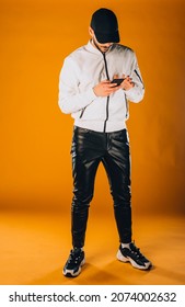 Cool young man dressed in white wind jacket posing in modern studio against orange background - Shutterstock ID 2074002632