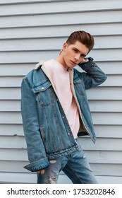 Cool Young Man With Serious Face With Trendy Hairstyle In Fashionable Blue Denim Casual Wear Posing Near Vintage White Wall On Street. Attractive Guy Model In Fashion Youth Jeans Clothes Enjoy Walk.