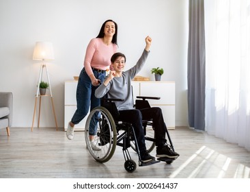 Cool Young Mom And Her Disabled Son In Wheelchair Having Fun At Home, Full Length. Cheerful Family With Mother And Impaired Teen Boy Playing, Being Silly Indoors. Parent Child Pastimes Concept