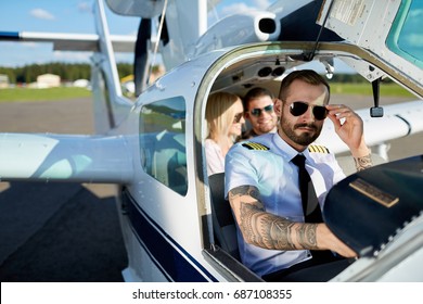 Cool Young Pilot And Happy Couple Sitting In Cabin Of Private Air Plane To Fly On A Vacation In Summer