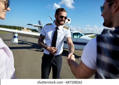 Cool Young Pilot In Uniform Welcomes Tourists Couple To Fly On Private Motor Air Plane. Summer Traveling Is Fun