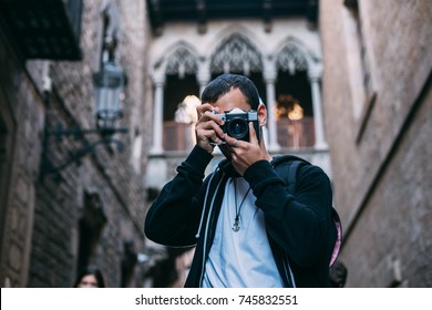 Cool Young Trendsetter, Male Tourist Explores New Culture Or City In Old European Town. Makes Photo On Vintage Analog Camera, To Prepare Content For Blog Post On Internet