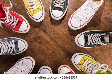 Cool Youth White Yellow Red Blue Black  Gym Shoes Standing In Circle  On Brown Parquet  Wooden Floor With Copy Place  Top View 