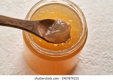 Cooled down congealed beef bone broth on a spoon and in a glass jar on a white background