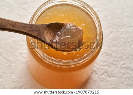 Cooled down congealed beef bone broth on a spoon and in a glass jar on a white background