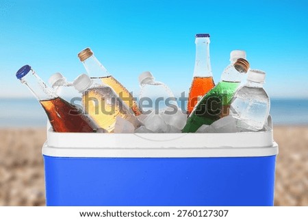 Cooler box with different drinks and ice on beach near sea