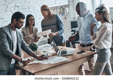 Cooperation in action. Group of young modern people in smart casual wear discussing business while standing behind the glass wall in the creative office - Shutterstock ID 1068846212