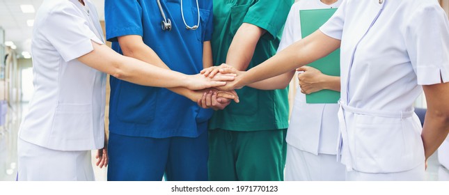 Cooperation Of People In The Medical Community Teamwork With A Hands Together Between The Doctor In The Green, Blue Uniform And Nurses In White Dress At Hospital. Fight Covid 19 Virus Healthy Concept.