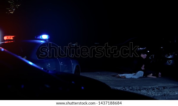 Cop getting out from patrol car and checking\
victim of crime lying on\
street