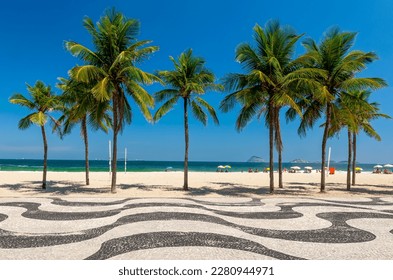 Copacabana beach with palms and mosaic of sidewalk in Rio de Janeiro, Brazil. Copacabana beach is the most famous beach in Rio de Janeiro. Sunny cityscape of Rio de Janeiro