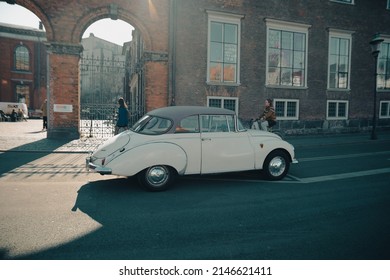 Copenhagen, Denmark - March 11, 2022: Image of an old Audi car on the street in front of a building in copenhagen. a lady rides by on a bicycle.