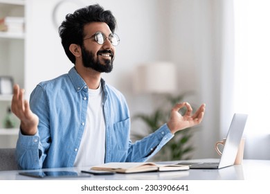 Coping With Working Stress. Portrait Of Smiling Calm Indian Man Meditating At Home Office, Handsome Eastern Male Freelancer Practicing Yoga While Sitting At Desk With Laptop Computer, Copy Space - Powered by Shutterstock