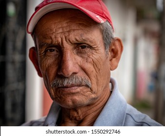 Copoya / Mexico - November 6, 2018: A Weathered Old Male Shop Keeper, With A Pink Baseball Cap, Looks At The Camera.