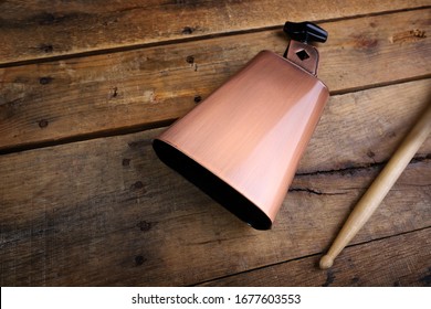 Copper Cowbell musical instrument on a wooden background with drumstick