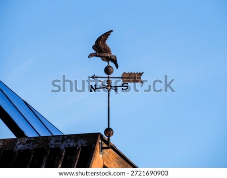 Copper eagle weather vane with compass points spinning on a roof under clear blue sky.