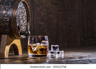 Copper Forged Barrel And A Glass Of Whiskey And Ice On A Old Table