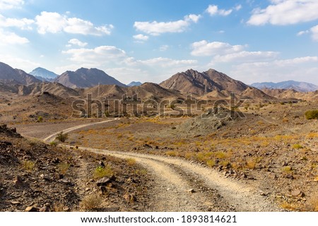 Copper Hike trail, winding gravel dirt road through Wadi Ghargur riverbed and rocky limestone Hajar Mountains in Hatta, United Arab Emirates. 