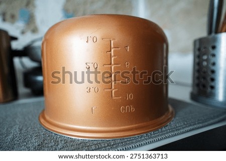 Copper Measuring Cup Upside Down Closeup With Embossed Measurement Marks And Warm Patina On Metal Surface, Shallow Depth Of Field Highlights Texture, Blurred Grater And Utensil Background On Rustic