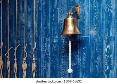 Copper Old Vintage Bell, Doorbell, Rope On A Wooden Blue Aged Wall. Concept Decor Element In Interior Of Deck, Cabin Of Ship, Restaurant, Room, House Decorated On The Marine Theme