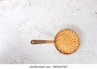 A copper pan of unpopped corn kernals on a white textured background with space for text, copyspace, popcorn day19  January 2021