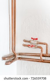 Copper Pipe With A Red Valve On A Background Of A White Wall