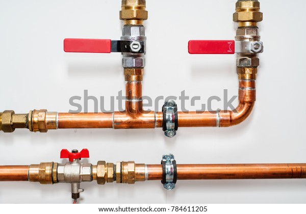 Copper pipes\
and valves on a white wall. Close\
up.