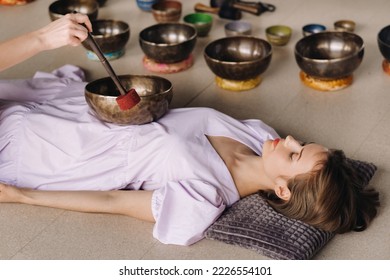 The copper singing bowl of the Nepalese Buddha in the spa. A young beautiful woman is doing a massage with singing bowls in a spa salon against the backdrop of a waterfall - Shutterstock ID 2226554101